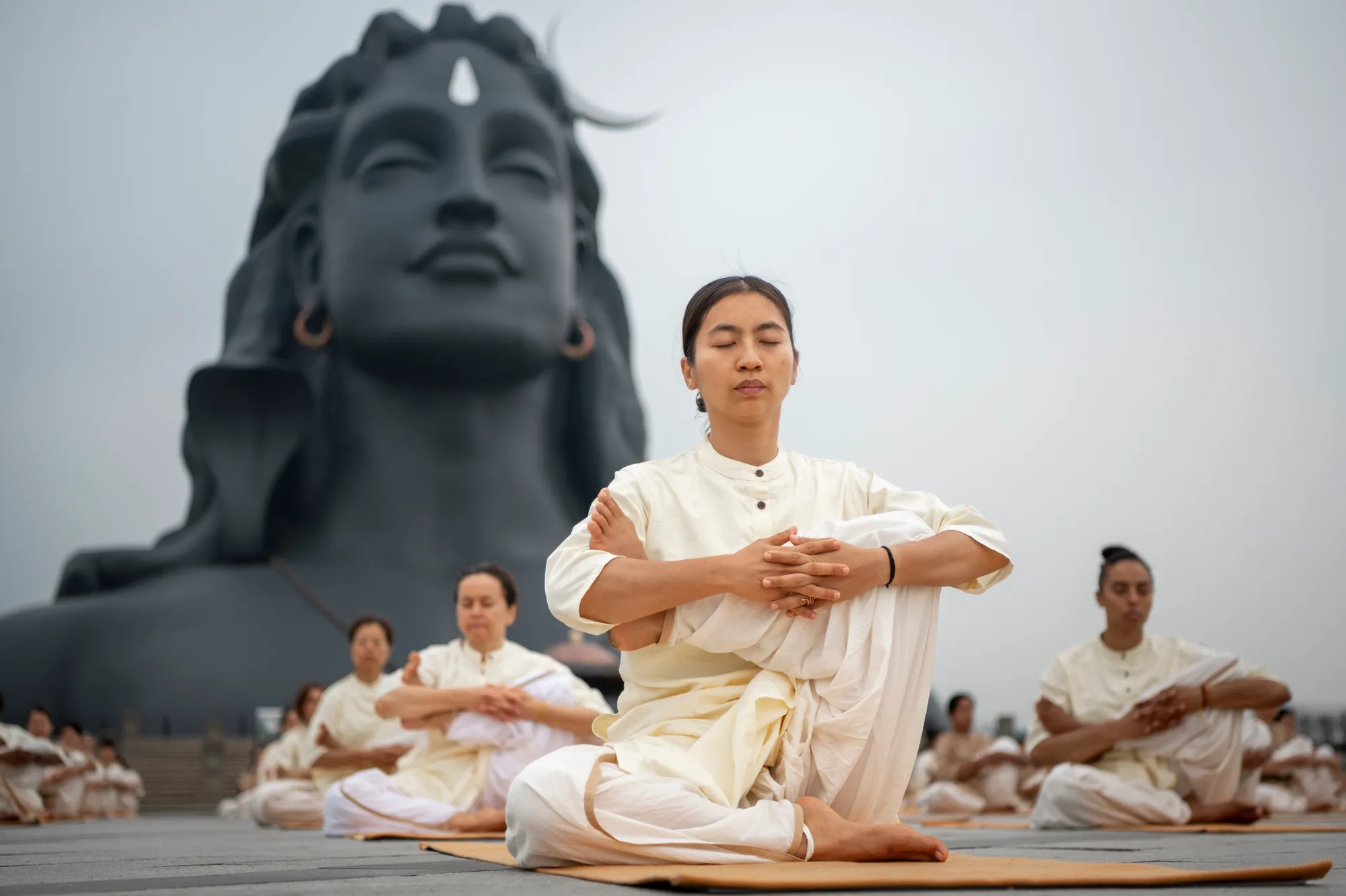 Practitioners in white sit in meditation before the Adiyogi, a large sculpted face of the first yogi.