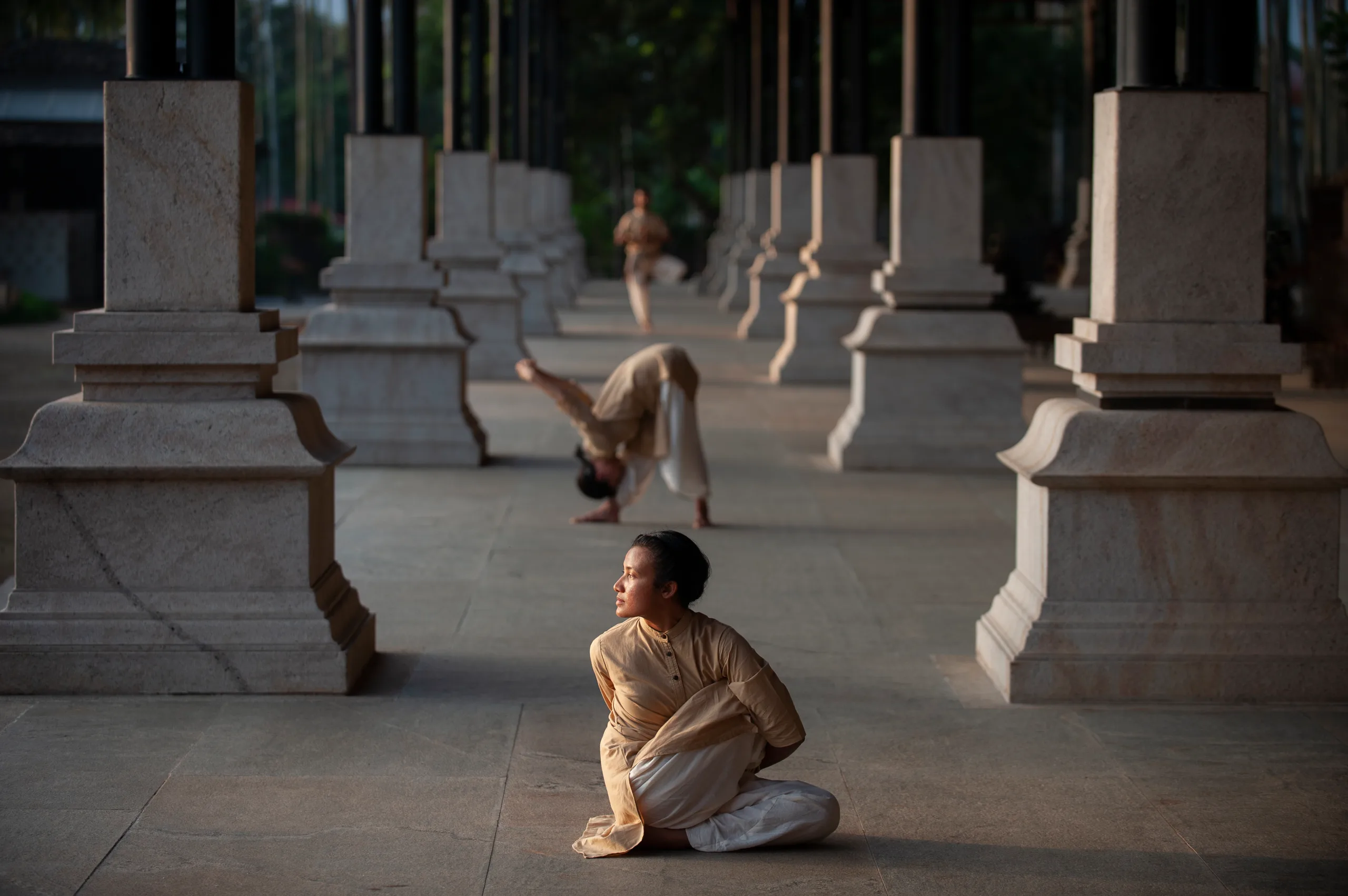 Practitioners hold classical postures along a sunlit stone colonnade at dawn.