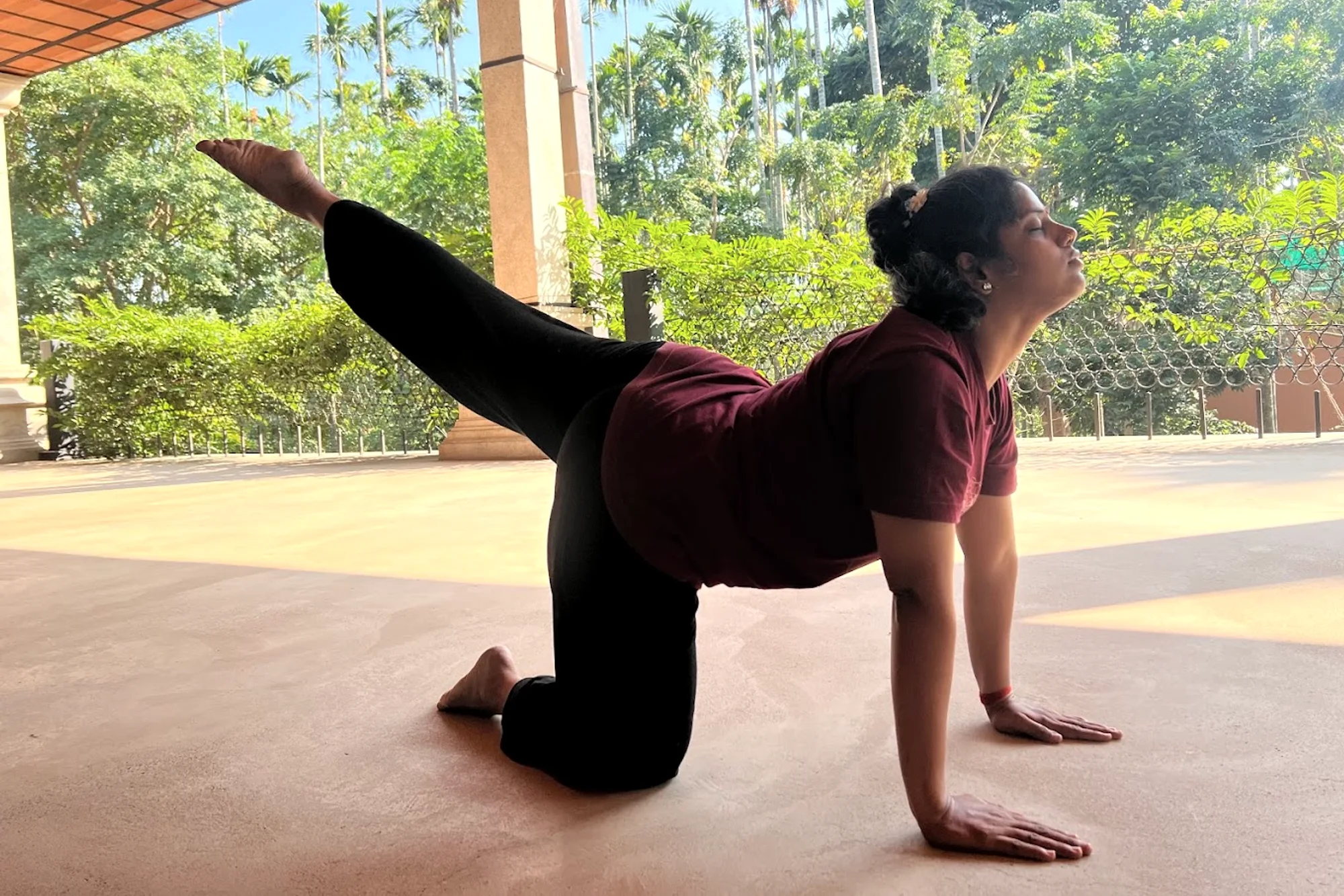 A practitioner holds a low posture on an open terrace beneath a colonnade, palms flat, gaze lifted.