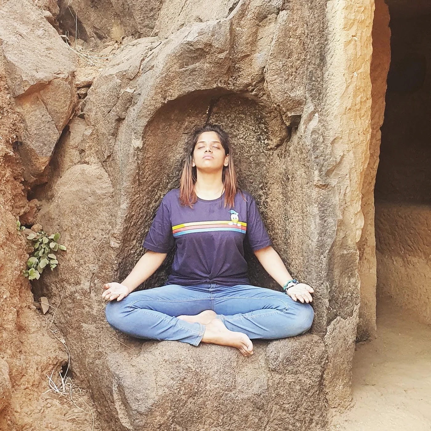 A practitioner sits cross-legged in meditation within a smooth hollow of rock.